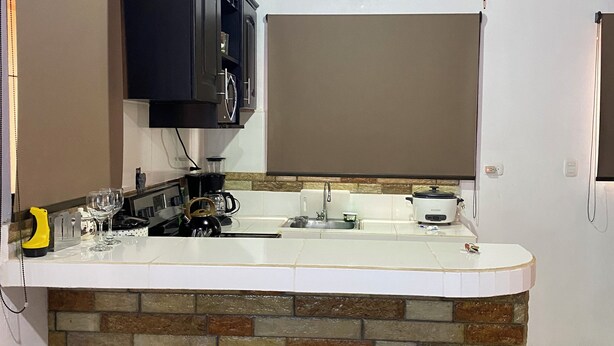 A kitchen with a stone island, two stools, a microwave, and a hanging television.