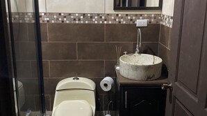 A bathroom with a toilet, bidet, sink, mirror, and tiled walls.