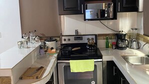 A compact kitchen with a stove, oven, microwave, and a coffee maker.