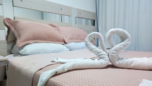 A neatly made bed with a pink blanket and pillows, and two white towels arranged in a swan shape on the bed. - Apartamento Prime Central (Curitiba)