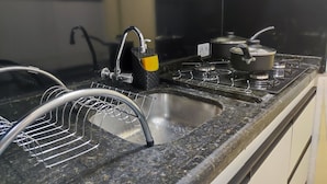 A kitchen with a black countertop, a stainless steel sink, a faucet, a stove, and a yellow soap dish. - Apartamento Prime Central (Curitiba)