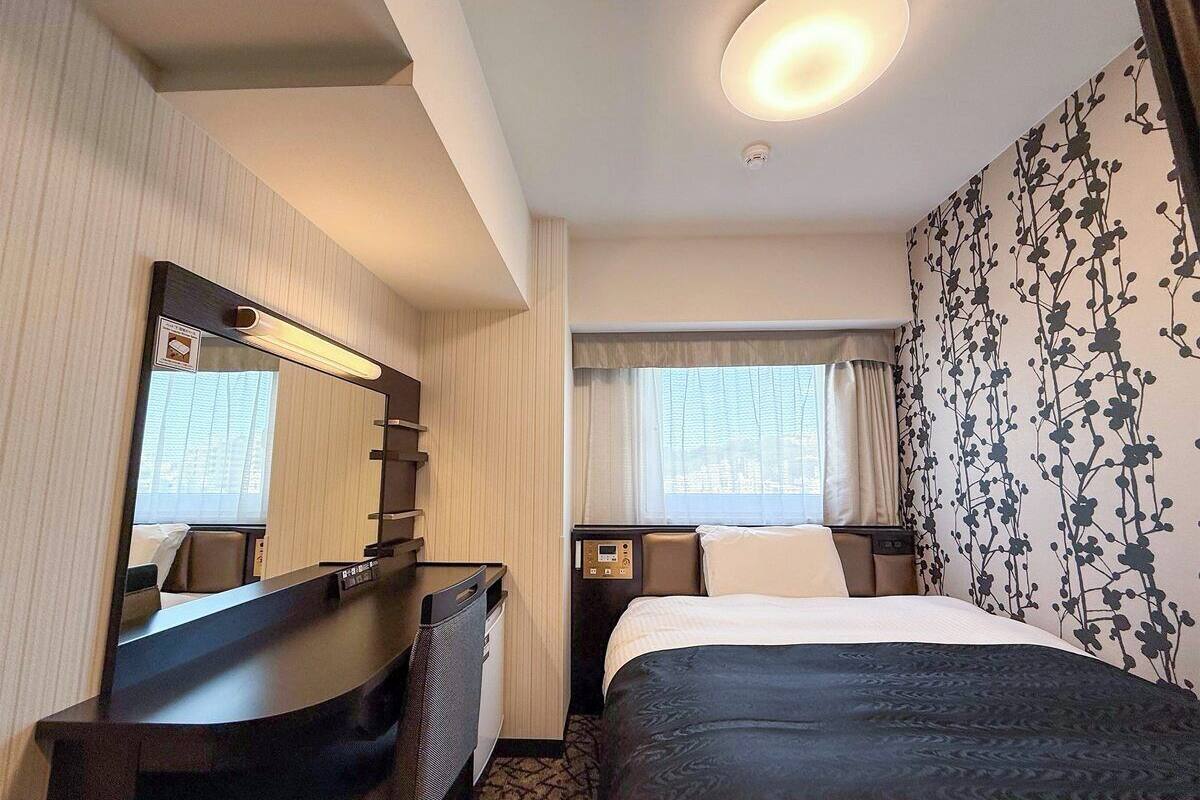 Ein Hotelzimmer mit Bett, Schreibtisch, Spiegel, Nachttisch und einem Fenster mit Vorhängen.