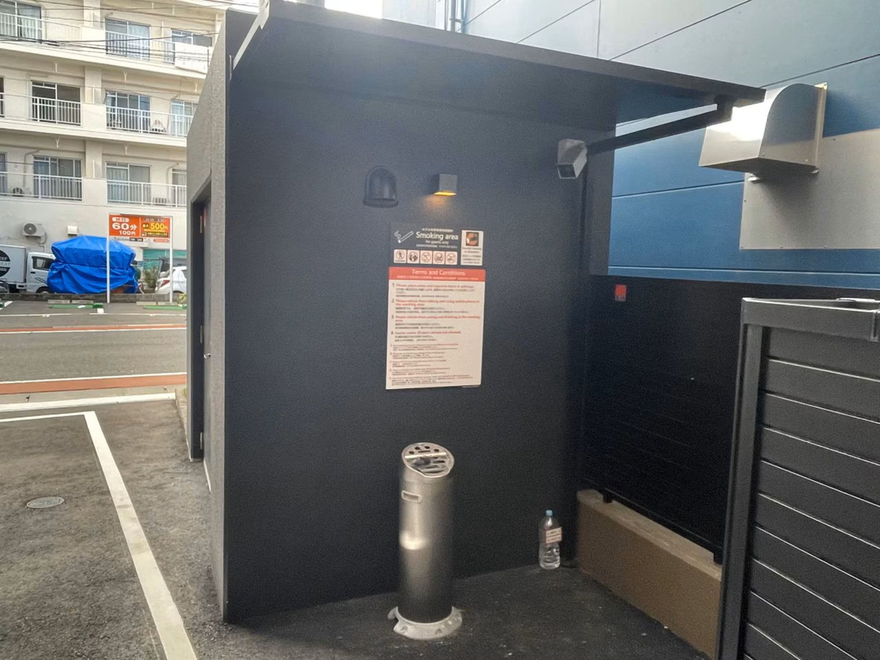A black metal structure with a sign indicating a smoking area, a water bottle, and a metal bollard.