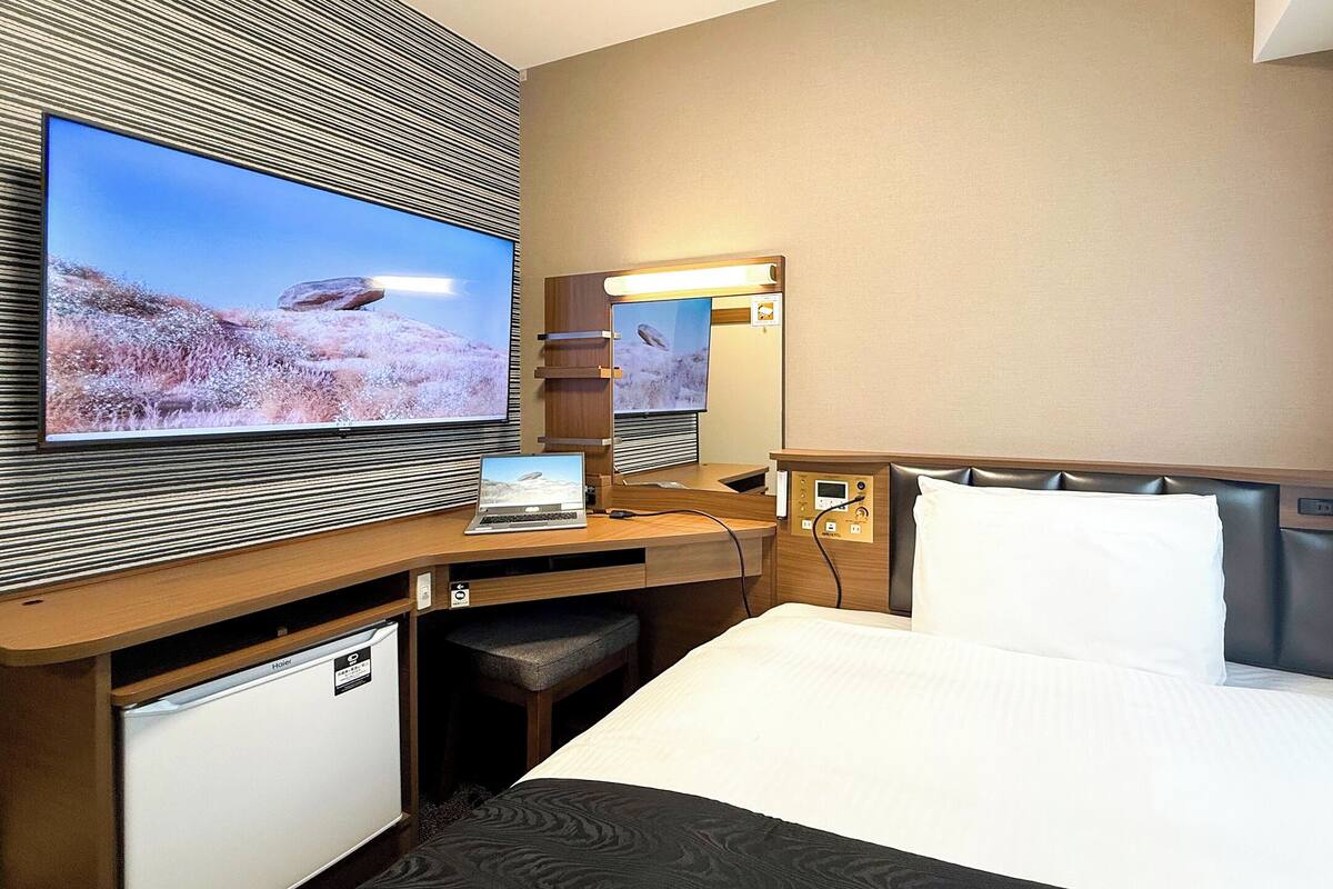 Ein Hotelzimmer mit einem Bett, einem Schreibtisch mit Laptop, einem Fernseher und einer Minibar.