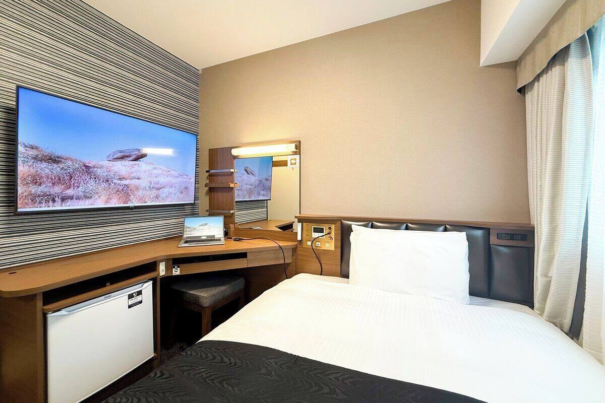 Ein Hotelzimmer mit einem Bett, einem Schreibtisch mit einem Laptop, einem Fernseher und einem kleinen Kühlschrank.