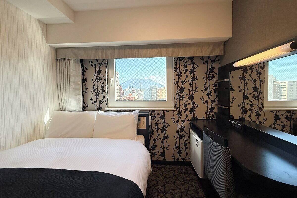 Ein Hotelzimmer mit Bett, Schreibtisch, Stuhl, Fenster mit Stadtblick und Spiegel.
