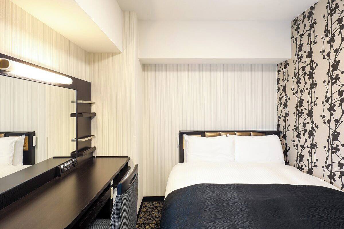 Ein Hotelzimmer mit Bett, Schreibtisch, Spiegel und Wand mit floralem Muster.