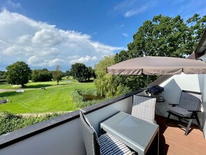 A balcony with a table and chairs, overlooking a golf course and a pond. - 3003 "maison Fleur-de-lis" - Wohnung 3003 am Schoor in Grömitz Inkl. Schwimmbadnutzung (Grömitz)