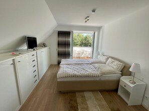 A bedroom with a bed, a desk, a chair, and a view of the outdoors. - 3003 "maison Fleur-de-lis" - Wohnung 3003 am Schoor in Grömitz Inkl. Schwimmbadnutzung (Grömitz)