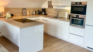 A modern kitchen with an island, built-in oven, and stainless steel appliances. - 3003 "maison Fleur-de-lis" - Wohnung 3003 am Schoor in Grömitz Inkl. Schwimmbadnutzung (Grömitz)