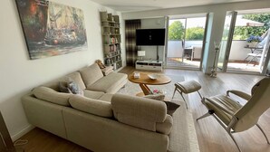 A living room with a sofa, a coffee table, a TV, and a bookshelf. - 3003 "maison Fleur-de-lis" - Wohnung 3003 am Schoor in Grömitz Inkl. Schwimmbadnutzung (Grömitz)