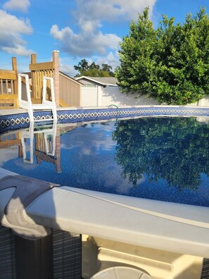 A swimming pool with a clear blue water surface, surrounded by a wooden deck and a tiled edge.