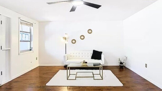 A spacious room with hardwood flooring, a white sofa, a glass coffee table, and a ceiling fan.
