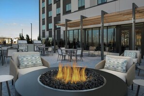 A modern outdoor seating area with a central fire feature, surrounded by wicker furniture and a glass building in the background. - Fairfield Inn & Suites by Marriott Paris (Paris)