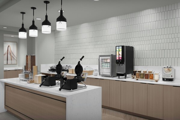 A modern kitchen area with a white countertop, a waffle maker, a coffee machine, and a refrigerator. - Fairfield Inn & Suites by Marriott Paris (Paris)