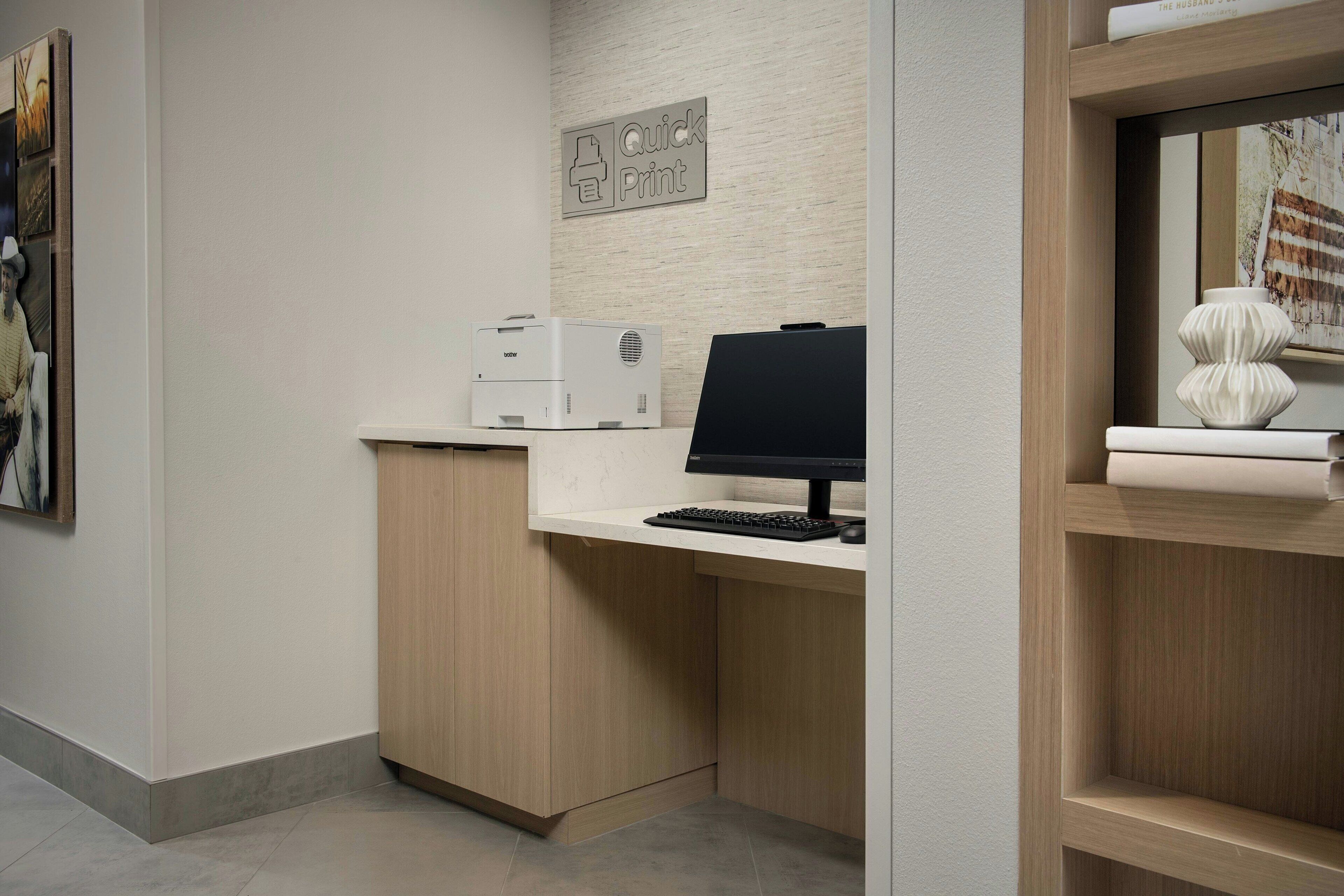 A modern office space with a desktop computer, a printer, and a framed picture on the wall.