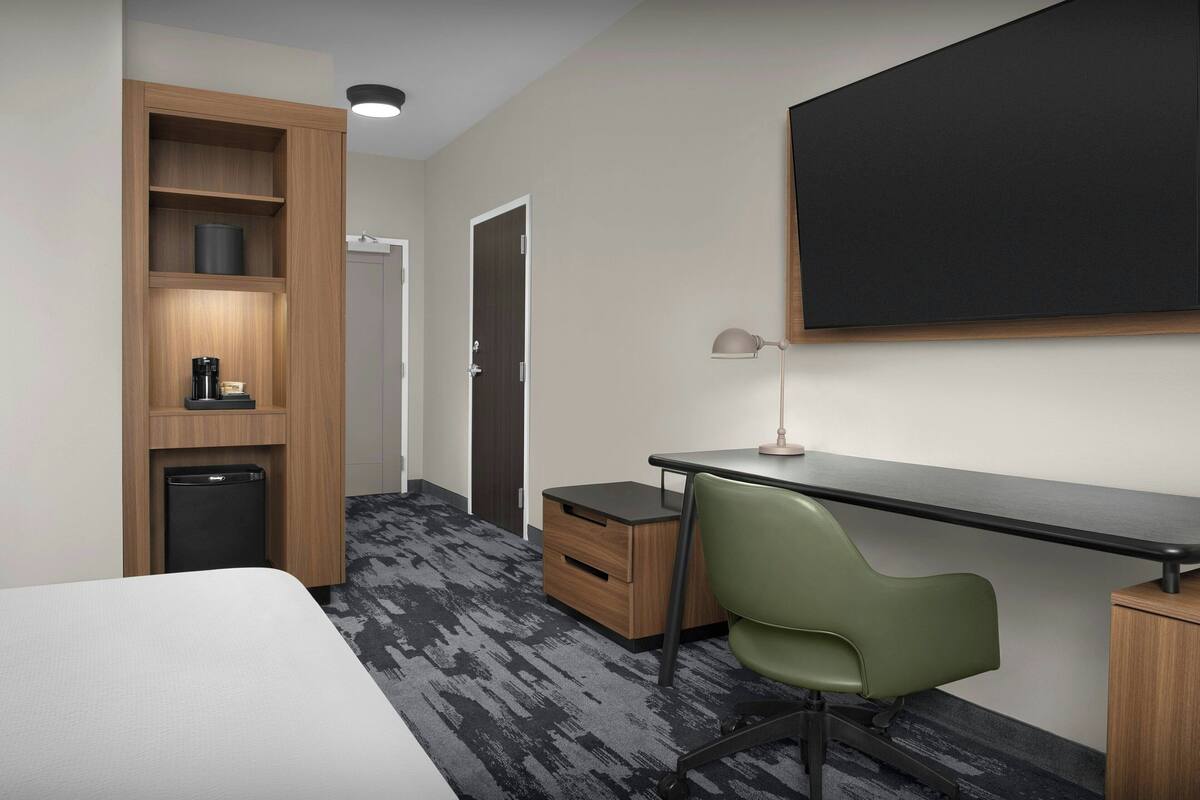 A hotel room with a bed, a desk with a chair, a wardrobe, a small trash bin, and a blackboard on the wall.