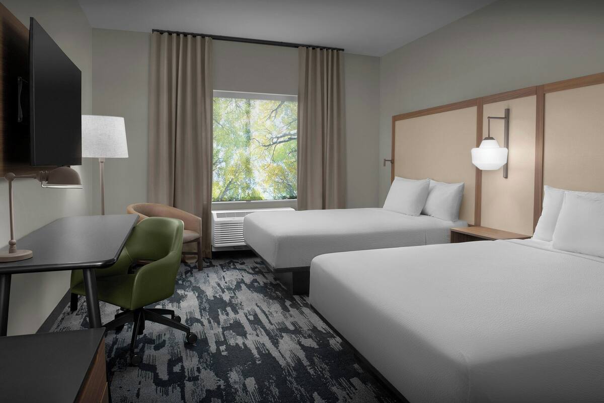 A hotel room with two beds, a desk with a chair, a TV, and a window with curtains.