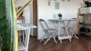Una habitación pequeña y acogedora con una mesa de comedor y sillas, una cafetera y un estante con utensilios de cocina.