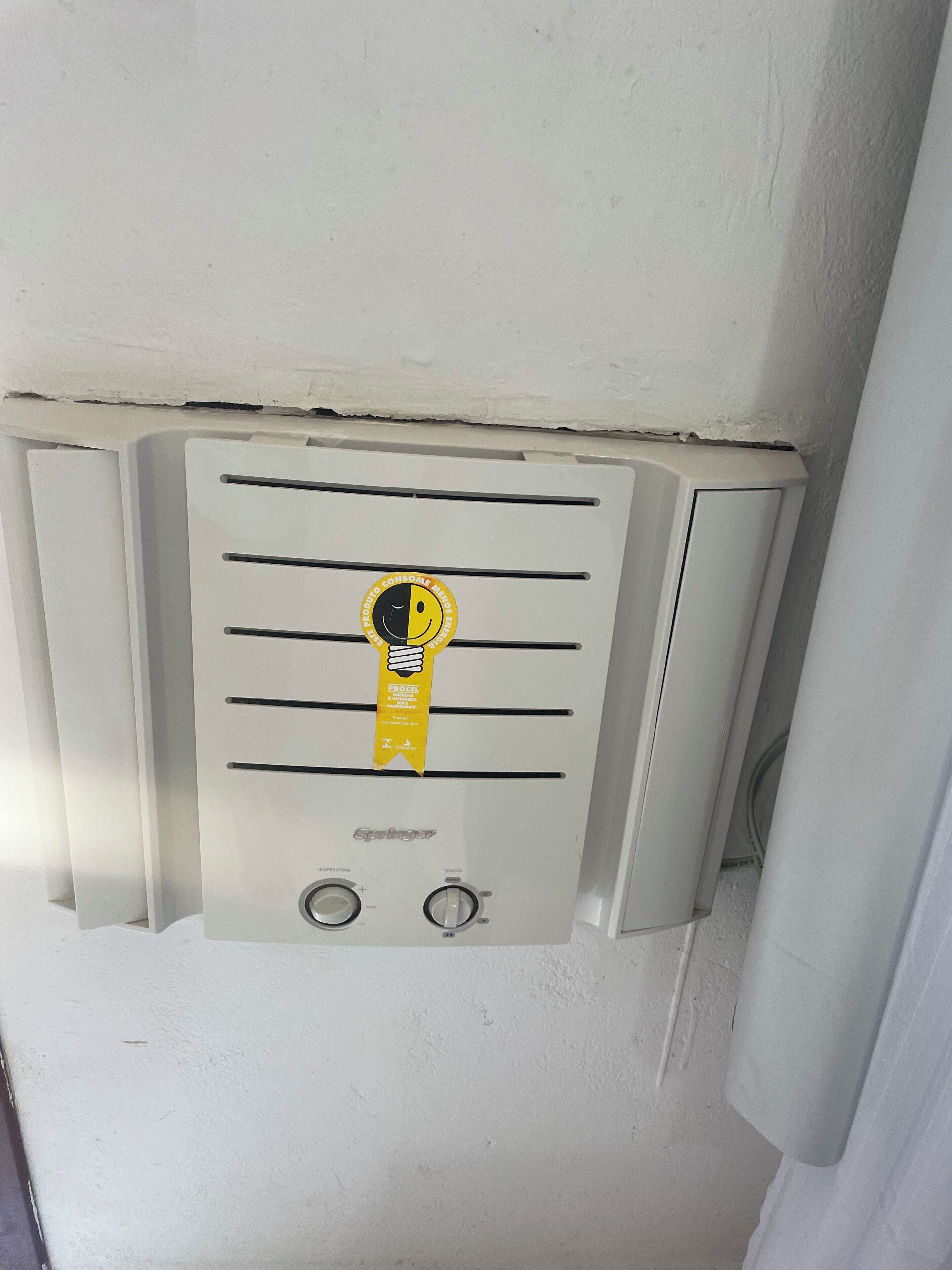 A wall-mounted air conditioning unit with a control panel and a yellow safety tag.