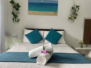A neatly made bed with a teal and white color scheme, a painting of a beach scene above it, and a small plant on the nightstand. - Suites Casa Azul-Vila do Abraão - conforto, limpeza, ótima localização (Angra dos Reis)