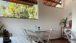 Una habitación con una mesa, sillas, una planta en maceta y vistas a un bosque a través de una ventana.