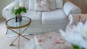 A white sofa with floral cushions, a glass coffee table, and a matching ottoman. - Liiger Wal - Typically Frisian: Apartment "Liiger Wal" in Morsum (Morsum)