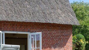 A brick house with a thatched roof, a patio with a table and chairs, and a garden with flowers. - Liiger Wal - Typically Frisian: Apartment "Liiger Wal" in Morsum (Morsum)