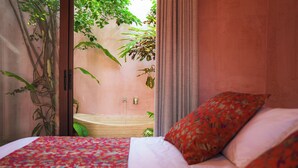Een slaapkamer met een bed, een badkamer zichtbaar door een open deur en uitzicht op groen buiten.