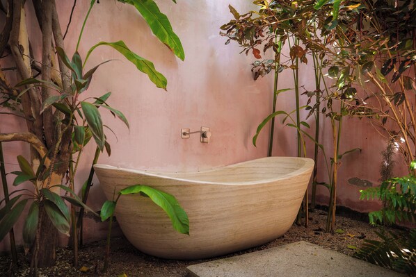 A large, wooden bathtub in a garden setting with various plants around.