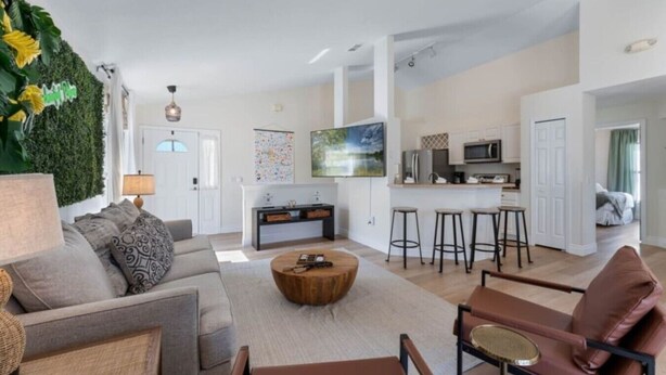 A modern living room with a sofa, coffee table, and a dining area with stools.