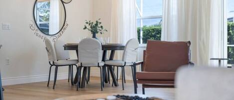 Uma sala de jantar com mesa, cadeiras, um candelabro e uma janela com cortinas.