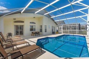 A covered outdoor swimming pool with lounge chairs, a table, and a covered patio area.
