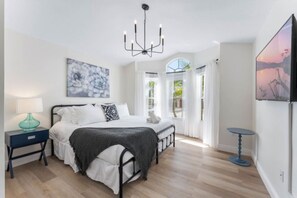 Una camera da letto con un letto, comodini, un lampadario, opere d'arte e vista dalla finestra.