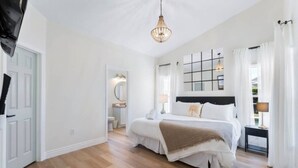 A bedroom with a large bed, a bedside table, a hanging light fixture, and a view of the bathroom.