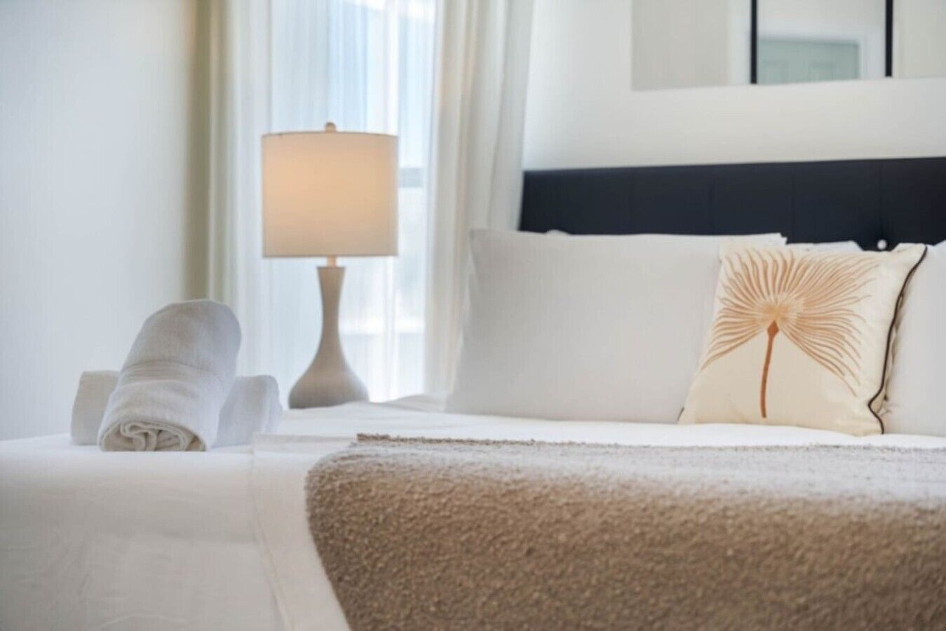 A neatly made bed with a white duvet, a decorative pillow, and a rolled towel on the side.