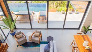 A spacious room with a large sliding glass door leading to a pool area. Inside, there is a sofa, a small round table, and a wooden dining table with chairs.