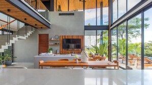 A spacious living area with a large flat-screen TV, a wooden dining table, and a staircase leading to an upper level.