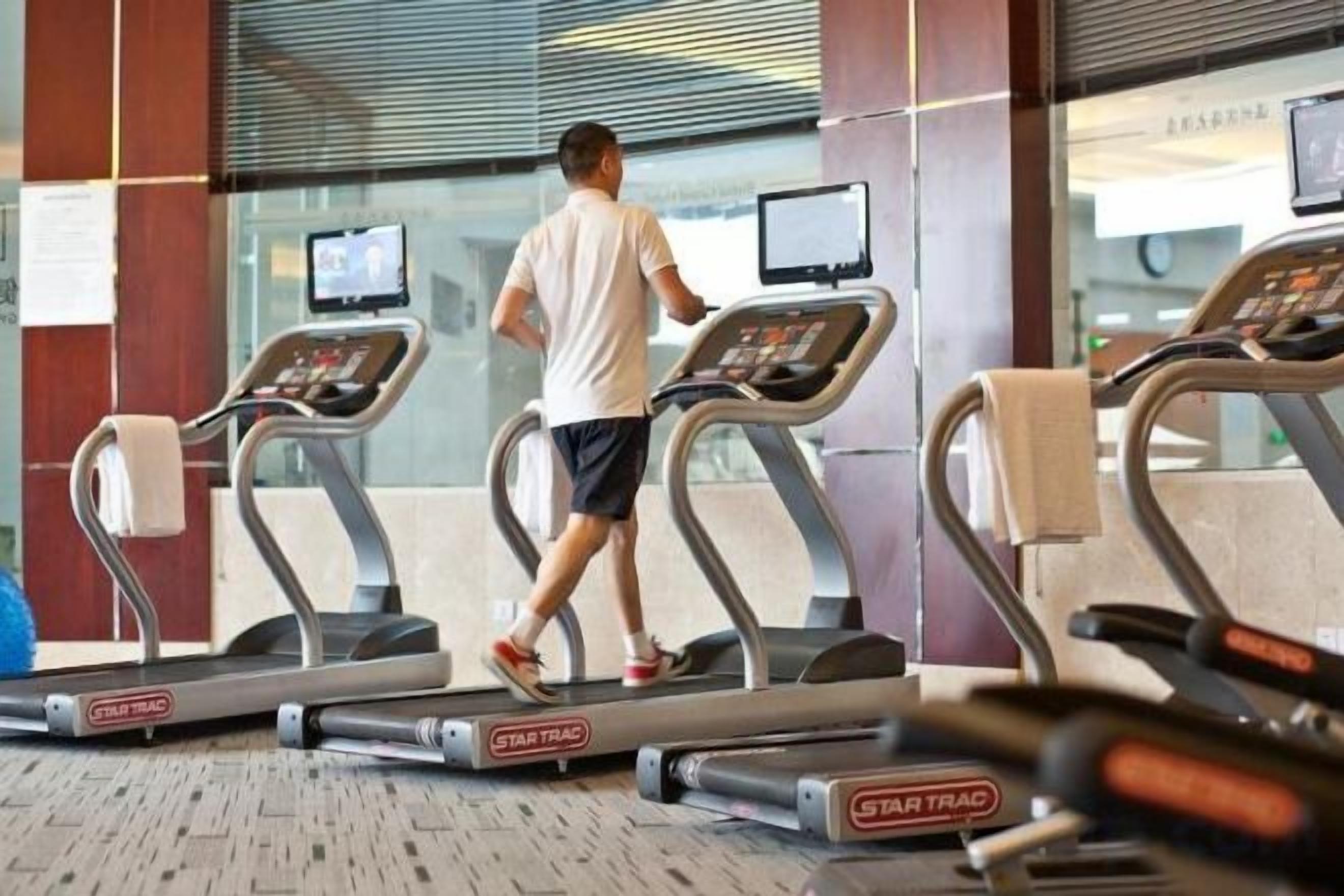 A person using a treadmill in a gym with multiple treadmills and digital displays.