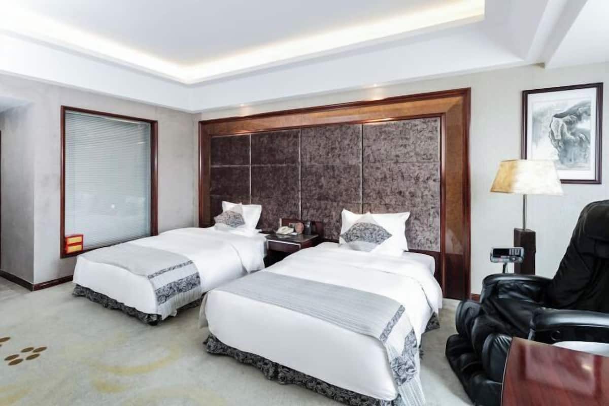 Une chambre d’hôtel avec deux lits, une grande tête de lit en bois, un bureau et un fauteuil en cuir.