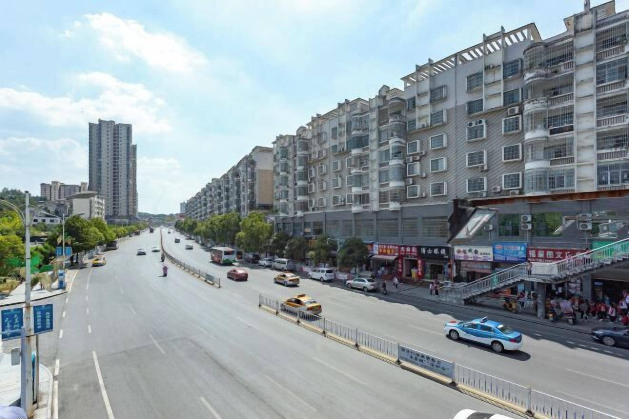A multi-story building with a commercial ground floor, a wide road with vehicles, and a tall building in the background.