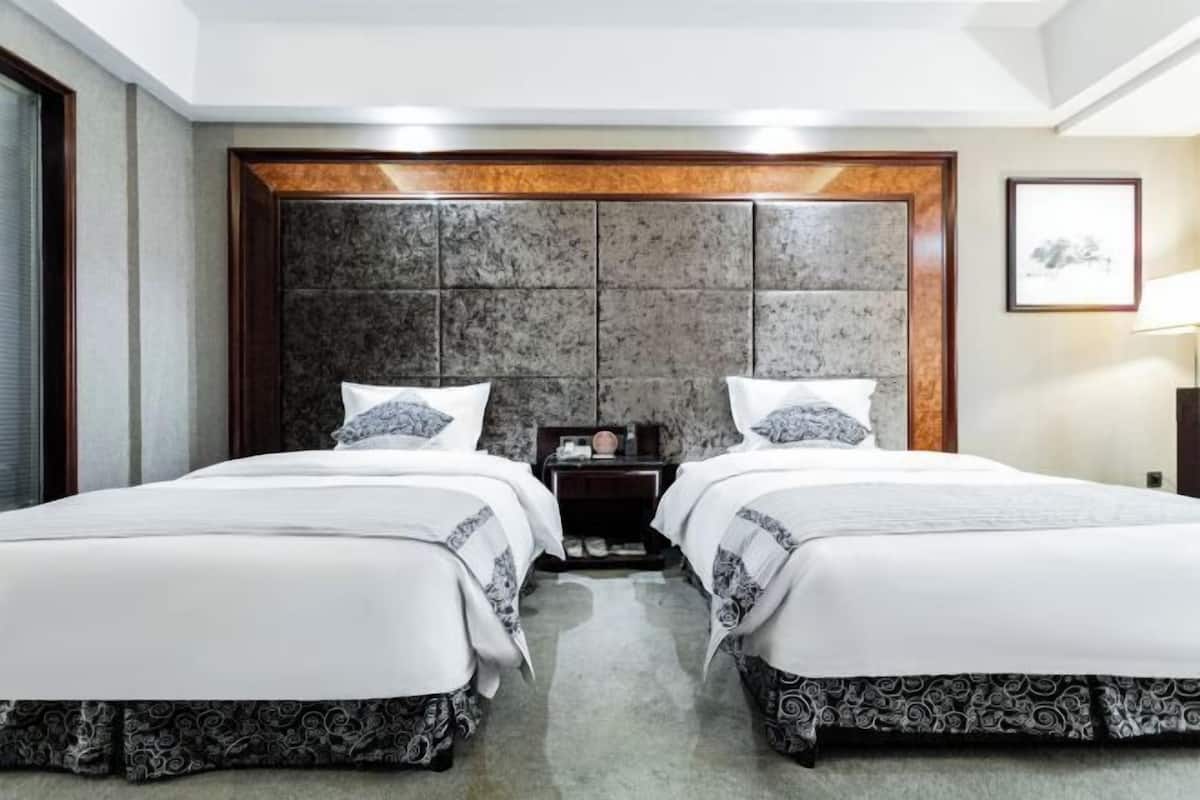 Une chambre d’hôtel avec deux lits, une tête de lit en marbre et un tableau encadré au mur.