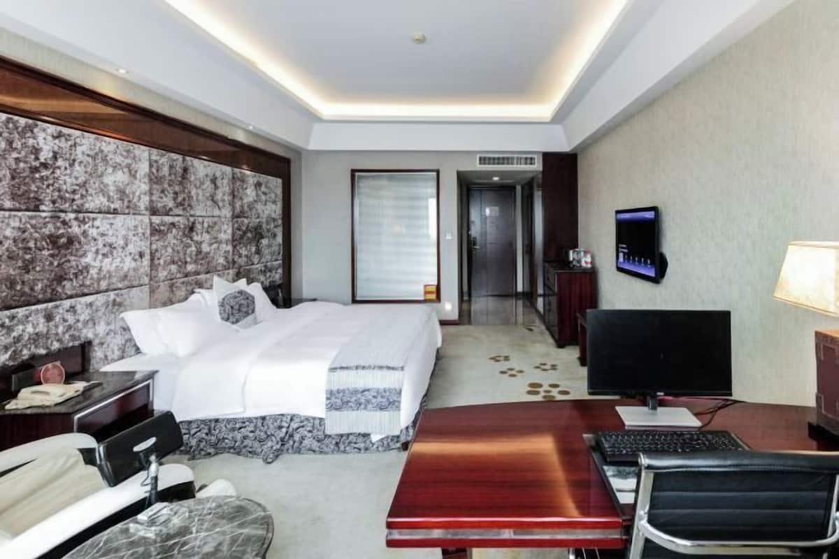 Une chambre d’hôtel avec un grand lit, un bureau avec un ordinateur, une télévision et une chaise.