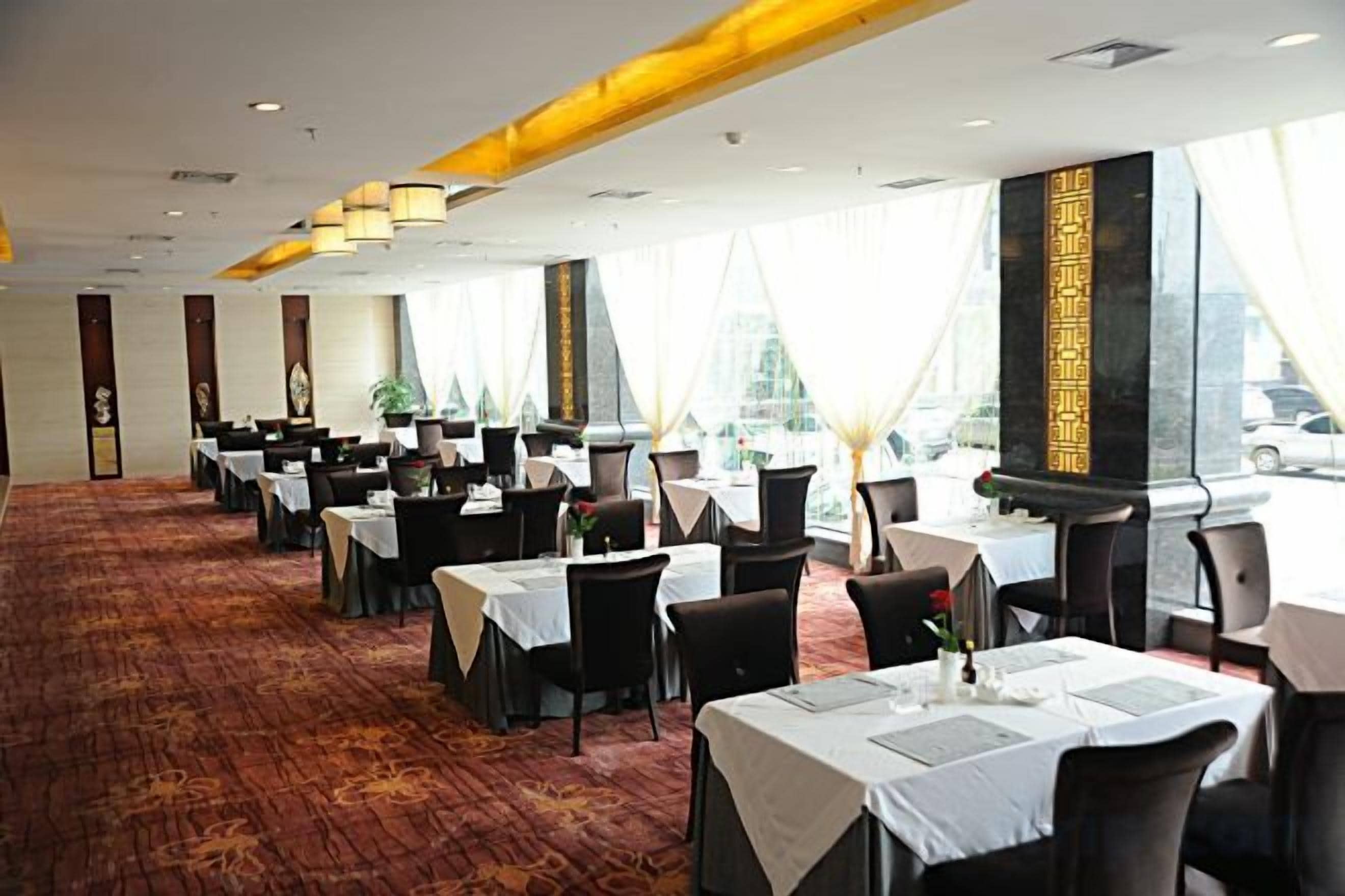 A spacious dining area with multiple tables and chairs, large windows, and a carpeted floor.