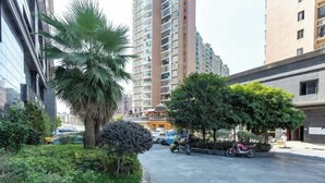 Une rue moderne en milieu urbain, avec un grand immeuble d’habitation, un palmier et une moto garée sur le trottoir.