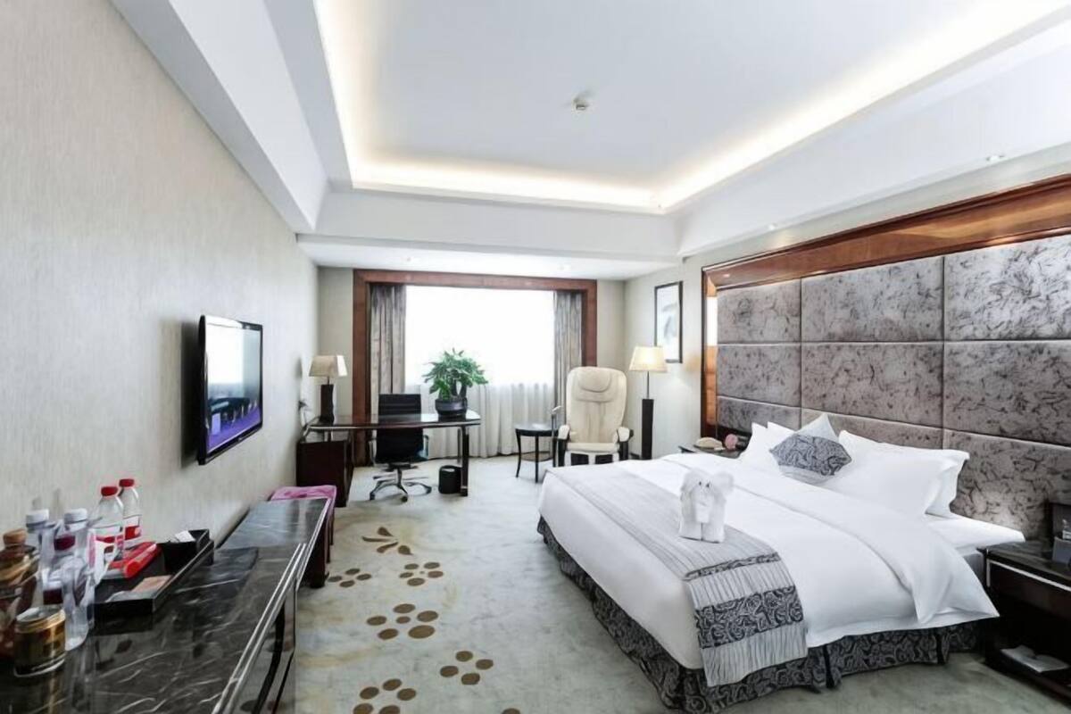Une chambre d’hôtel équipée d’un lit, d’un bureau, d’une chaise, d’une télévision et offrant une vue sur l’extérieur.