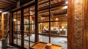 Una habitación de estilo japonés tradicional con suelo de tatami, una mesa de madera baja y vistas a través de amplios puertas correderas a un dormitorio con cama y mesitas de noche.