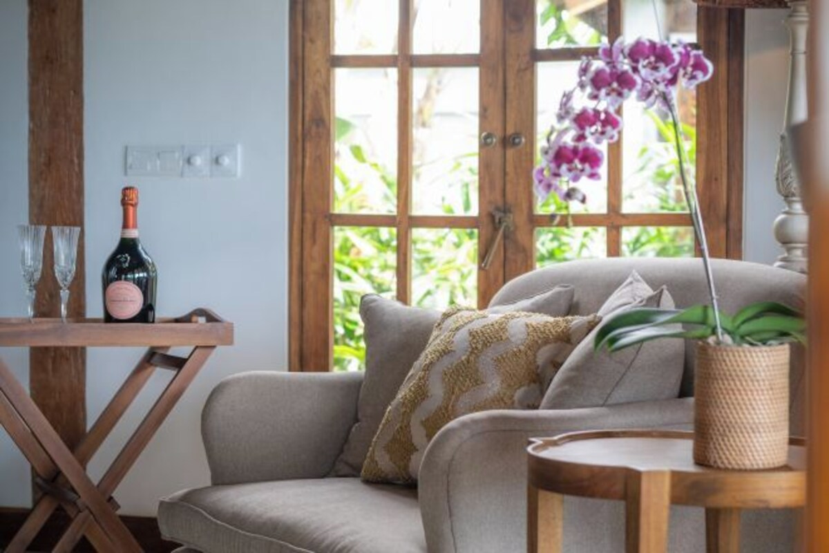 A cozy living area with a sofa, a small table, a bottle of wine, and a potted orchid.