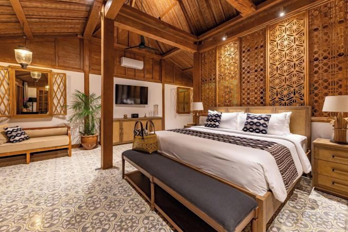 A room with a bed, bench, TV, and decorative panels.