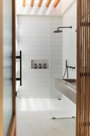 Une salle de bain moderne avec des murs recouverts de carreaux blancs, un espace douche et un meuble-lavabo doté d’un évier et d’un miroir.